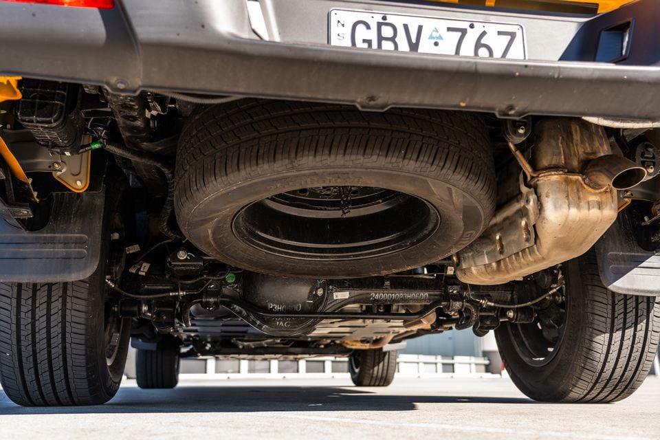 Underside of a JAC Hunter PHEV showing the spare wheel, exhaust system, rear axle and suspension components, with a NSW licence plate visible