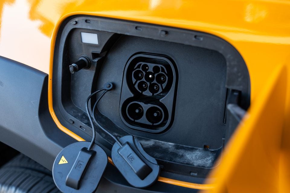 Close-up of the CCS combo charging port on a yellow JAC Hunter PHEV, with AC and DC port caps hanging open