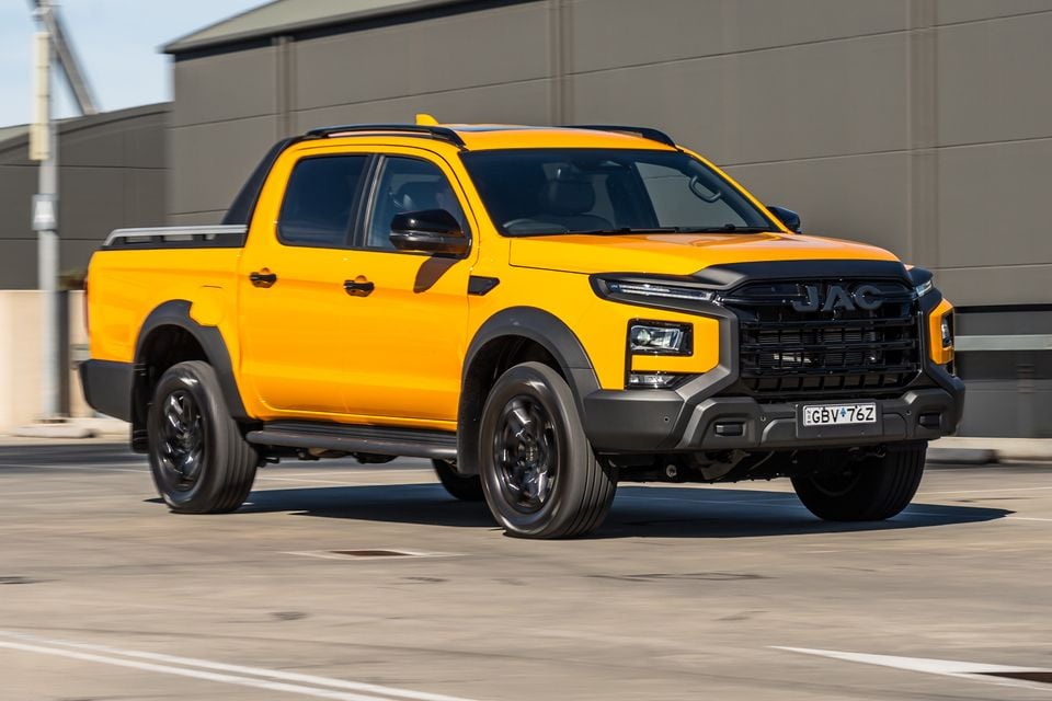 A yellow JAC Hunter PHEV dual-cab ute seen from the front-side angle, driving through a car park