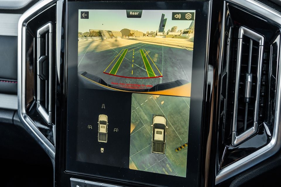 A car infotainment touchscreen displaying a rear-view camera feed with parking guidelines and a 360-degree bird's-eye surround view, inside a JAC Hunter PHEV