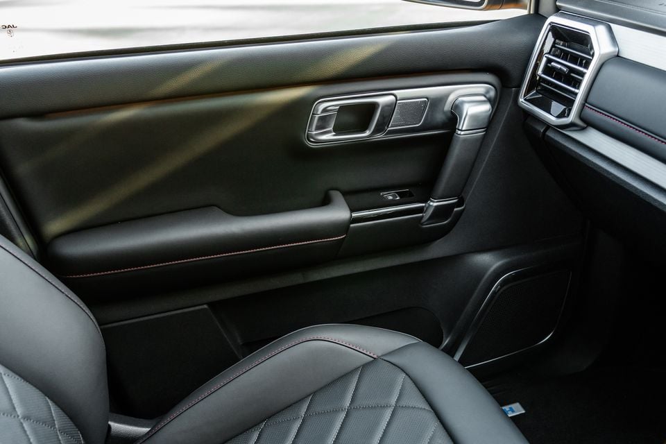 Interior view of a JAC Hunter PHEV showing the passenger door panel with chrome trim, diamond-stitched dark leather seats with red contrast stitching, and rear air vents