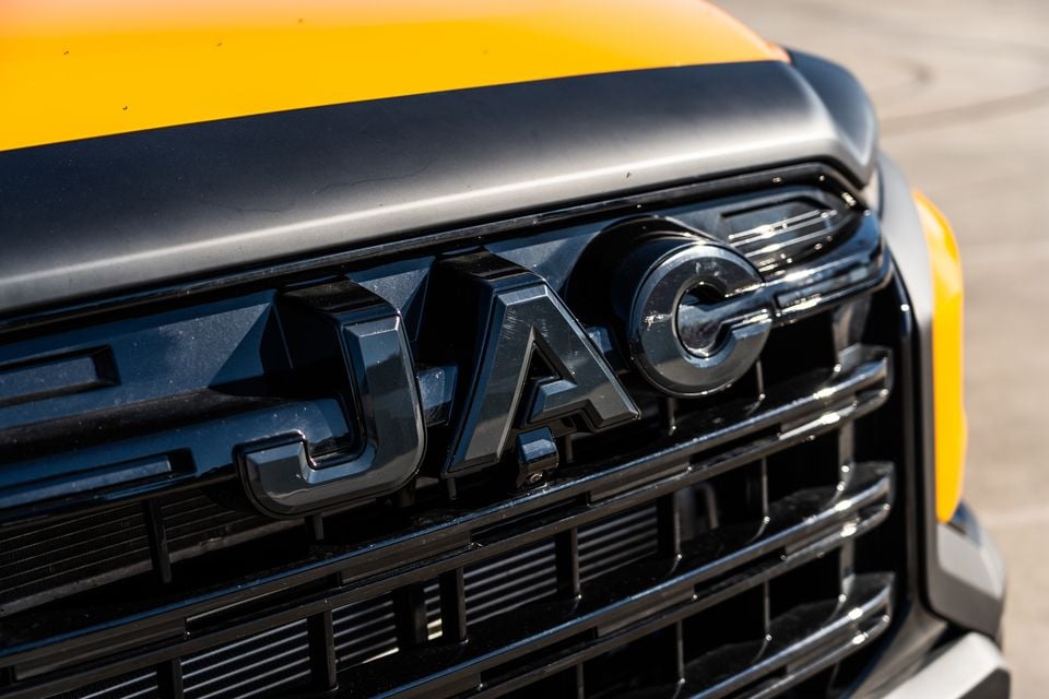 Close-up of the JAC badge on the front grille of a yellow JAC Hunter PHEV