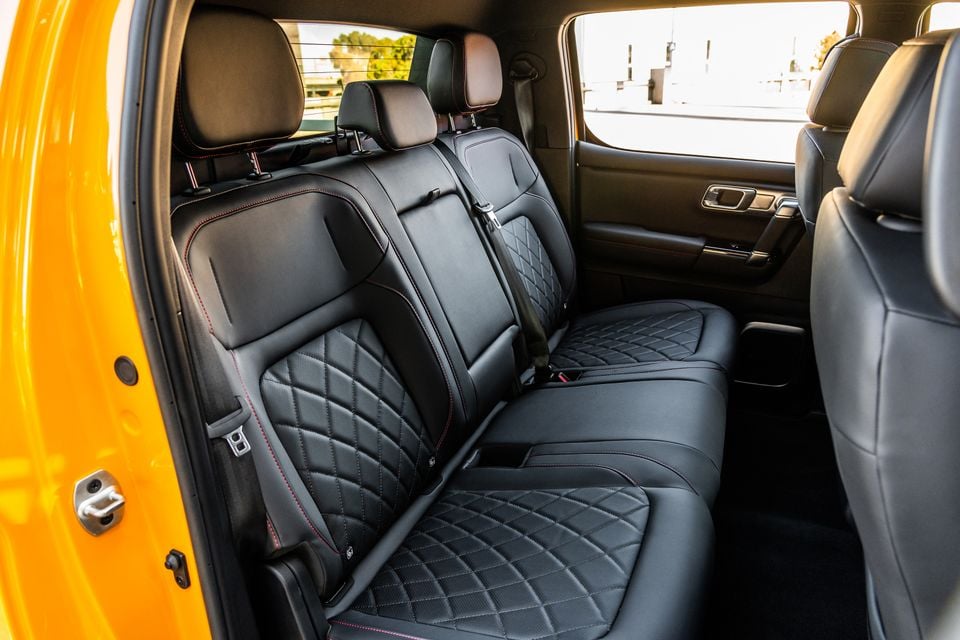 The rear seat interior of a JAC Hunter PHEV ute, showing black quilted leather bench seats with red contrast stitching and a yellow exterior door panel visible on the left.