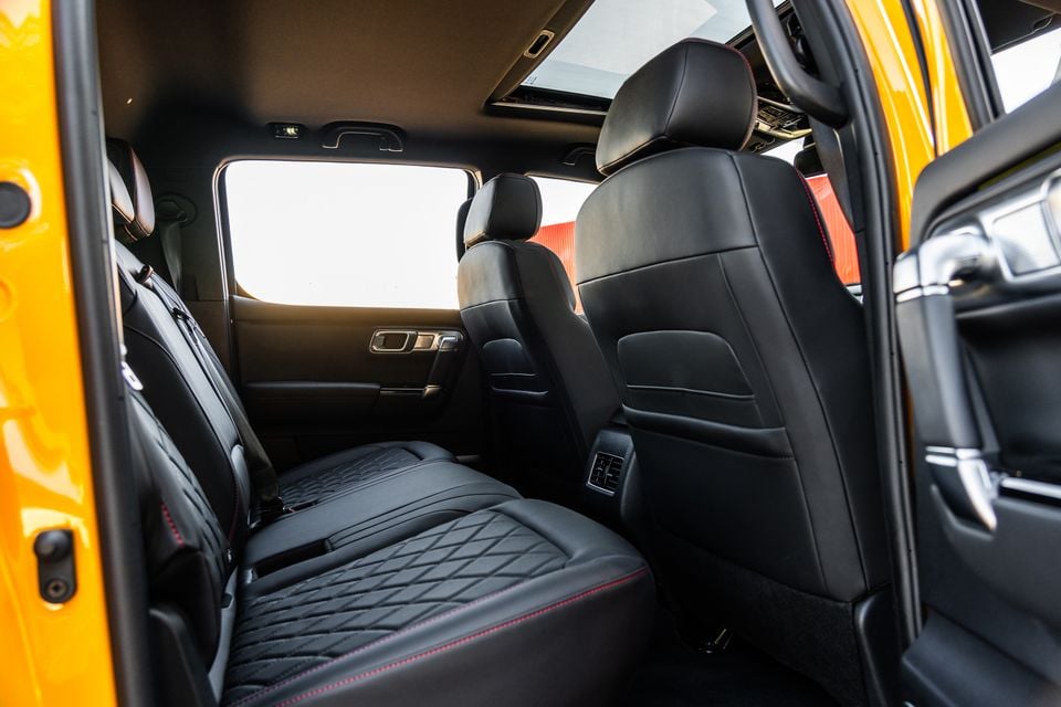 The rear seat interior of a 2026 JAC Hunter PHEV, showing black leather seats with diamond-stitched upholstery and red contrast stitching, rear climate vents, and a panoramic sunroof above