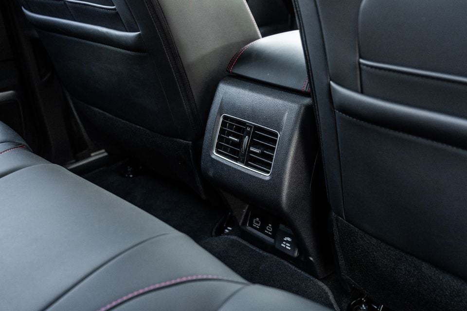 Rear passenger area of a 2026 JAC Hunter PHEV showing the rear air vents on the centre console and charging ports, with black leather seats featuring pink stitching