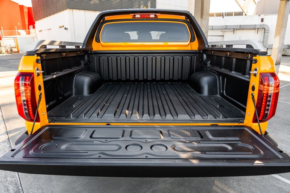 The open tray of an orange JAC Hunter PHEV ute, viewed from the rear with the tailgate down, showing the lined tub interior