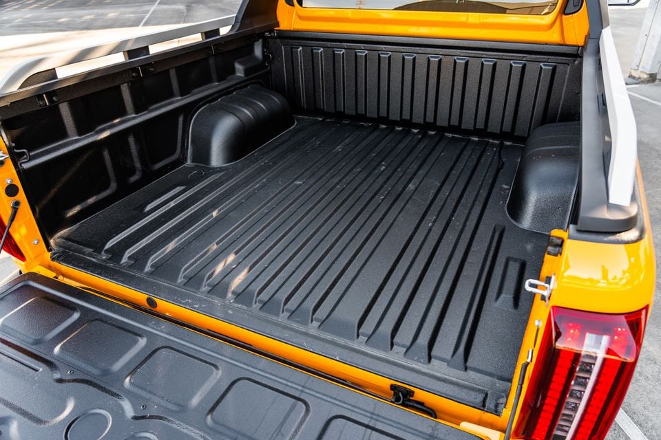 The open tray bed of an orange ute, showing a black plastic tub liner, ribbed floor, and lowered tailgate
