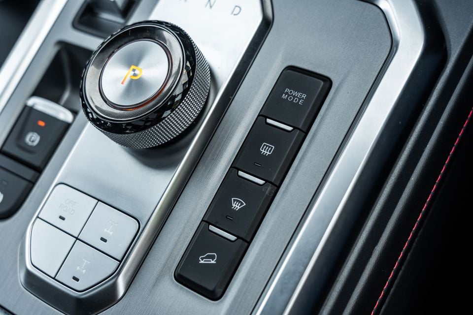 Close-up of the centre console controls in a 2026 JAC Hunter PHEV, showing a rotary gear selector in Park, off-road mode buttons, power mode button, and heated rear window and windscreen switches