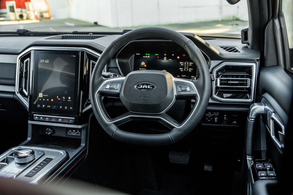 Interior of a JAC Hunter PHEV showing the steering wheel with JAC logo, large touchscreen infotainment display, digital instrument cluster, and centre console