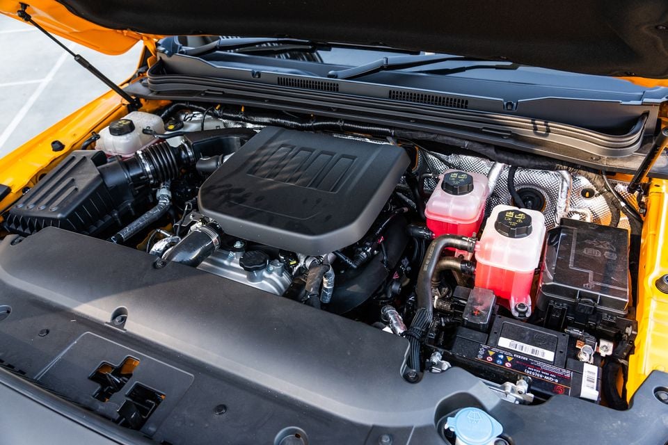 Engine bay of a yellow JAC Hunter PHEV showing the engine cover, battery, brake fluid reservoir and coolant reservoir with the bonnet open