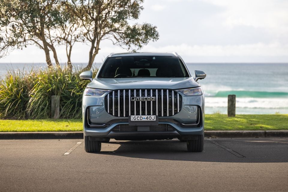 A silver Jaecoo J8 SUV seen from the front, parked near a coastal road with ocean views in the background.