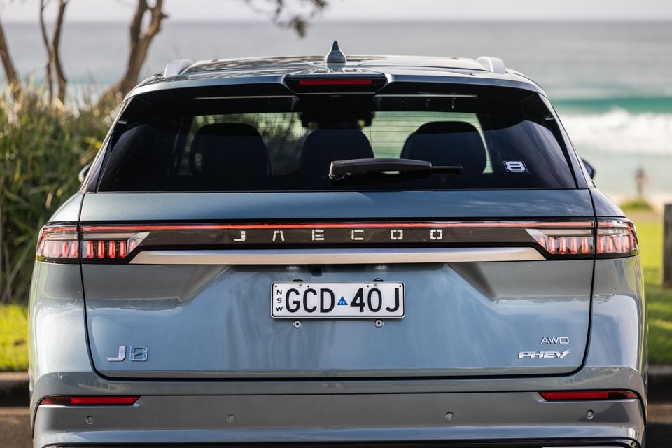 Rear view of a grey Jaecoo J8 AWD PHEV SUV with a NSW number plate, parked near a beach