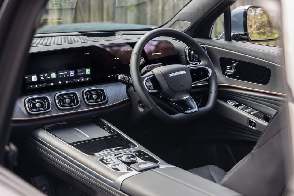 Interior of a Jaecoo J8 showing the dashboard, large touchscreen infotainment display, digital instrument cluster, steering wheel, and centre console