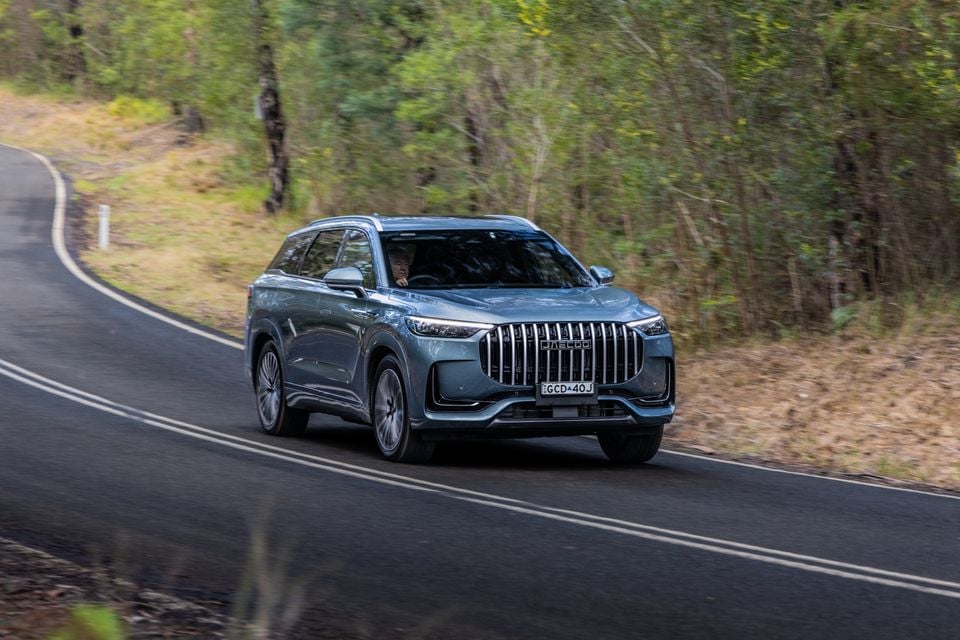 A grey Jaecoo J8 SUV driving along a winding road surrounded by bushland, seen from the front