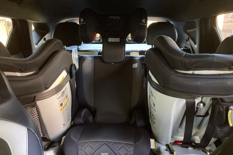 Three child car seats fitted across the rear seat row of a car, including two rear-facing infant seats on the outer positions and a forward-facing booster seat in the centre