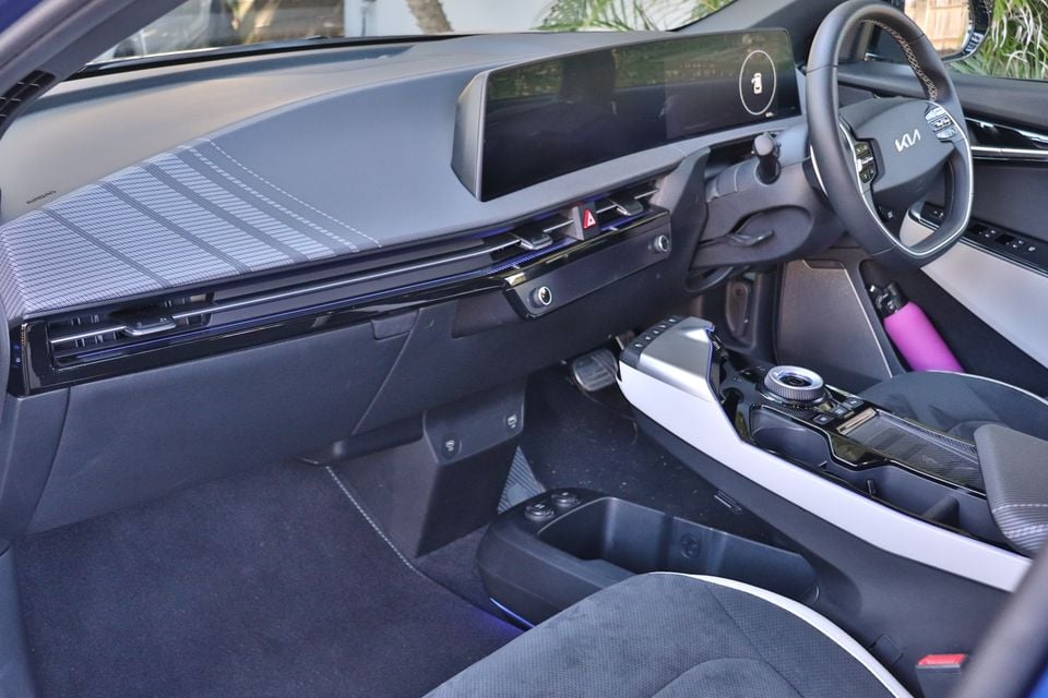 Interior of a Kia EV6 showing the dashboard, wide curved infotainment screen, centre console, and steering wheel from the passenger side
