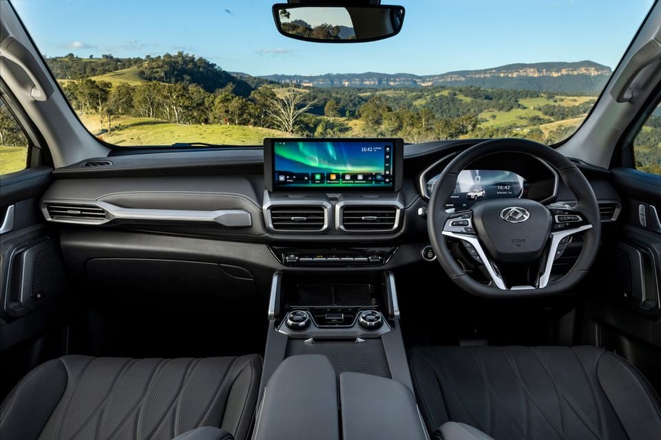 The black leather dashboard and steering wheel of a 2026 LDV D90 Luxe diesel SUV, with rolling green hills visible through the windscreen.
