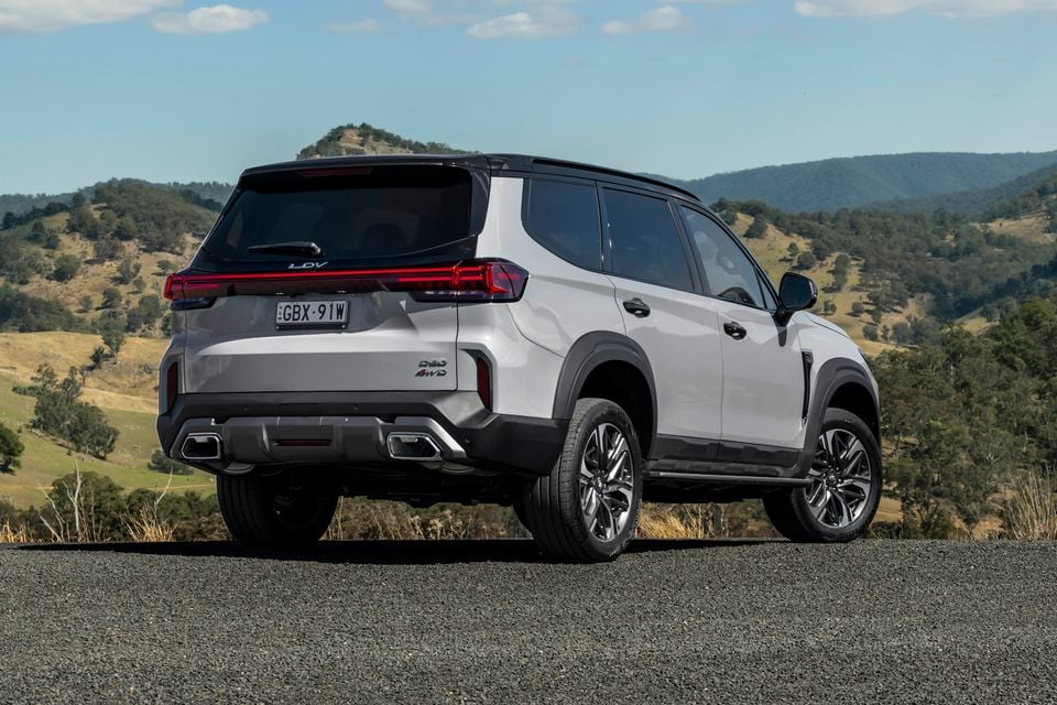 A white 2026 LDV D90 Luxe diesel SUV parked on a road with hills in the background, viewed from the rear quarter.