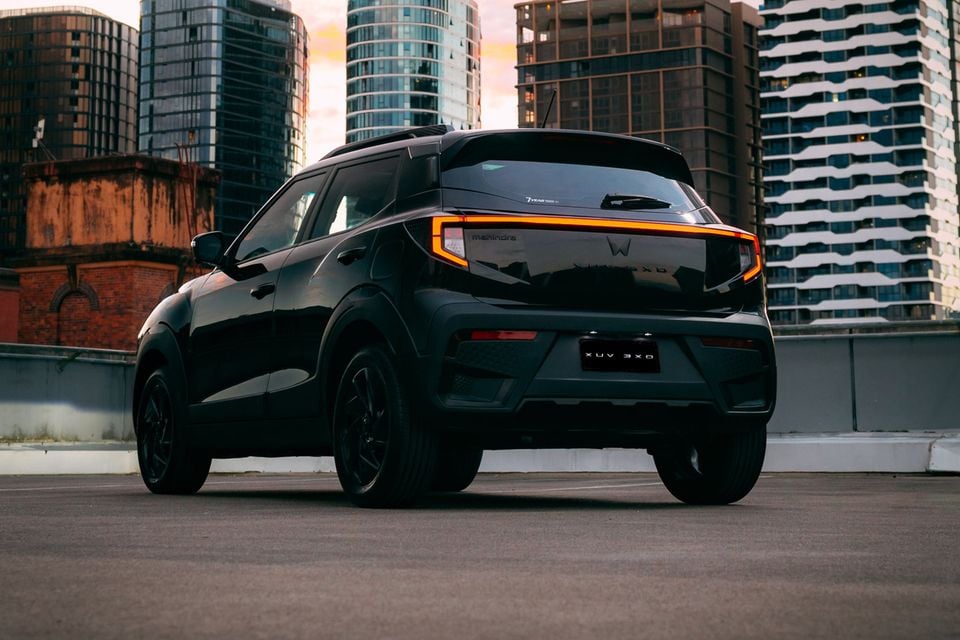 A black Mahindra XUV 3XO small SUV seen from the rear three-quarter angle on a rooftop car park with city buildings in the background at dusk.
