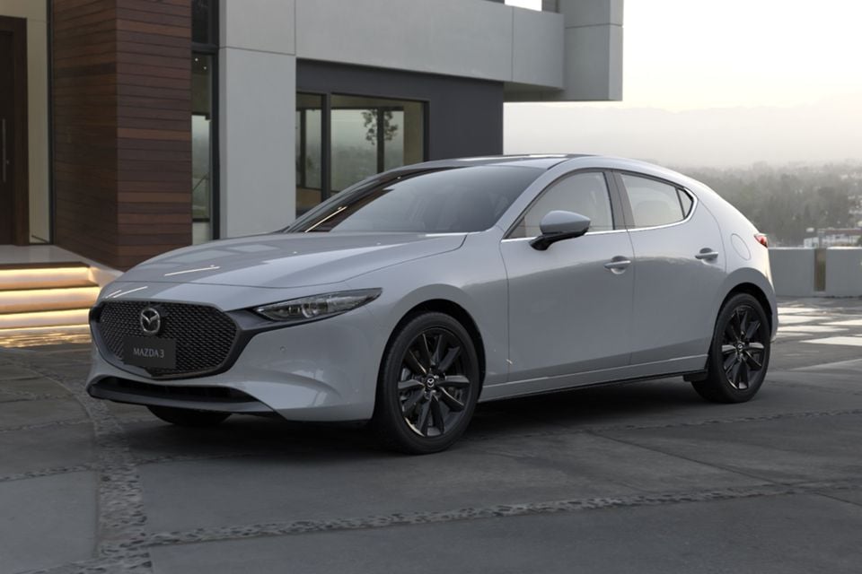 A silver 2026 Mazda3 hatchback with black alloy wheels parked outside a modern house, seen from the front left side