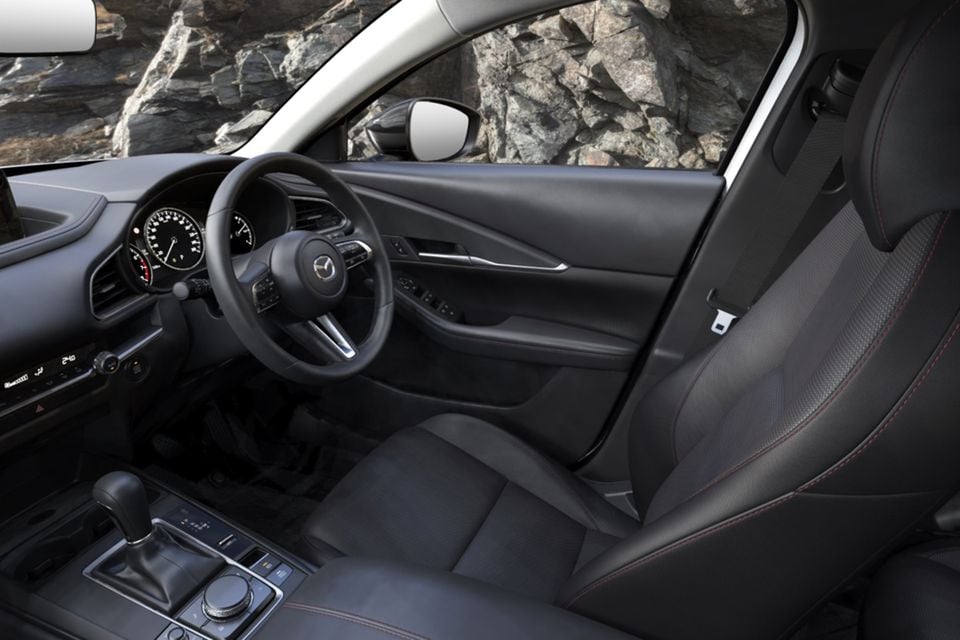 Interior of the 2026 Mazda CX-30 Evolve SP showing the steering wheel, instrument cluster, centre console and black front seats with red stitching
