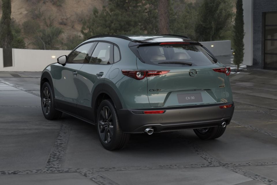 A green 2026 Mazda CX-30 G25 GT SP small SUV parked on a paved courtyard, seen from the rear left