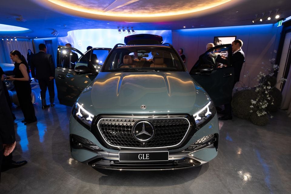 A Mercedes-Benz GLE SUV on display at an indoor launch event, seen from the front, finished in a sage green colour