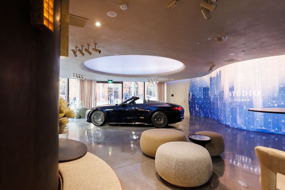 A dark blue Mercedes-Maybach convertible on display inside the Mercedes-Benz Studio Sydney showroom, surrounded by modern lounge seating and a branded feature wall.
