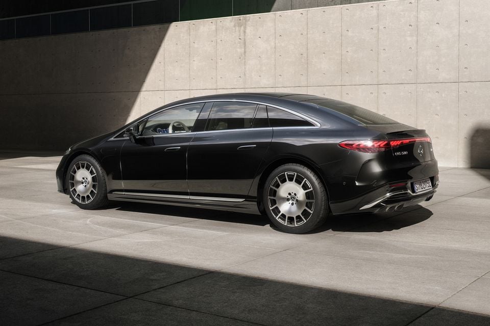 A black Mercedes-Benz EQS 580 sedan seen from the rear three-quarter angle, parked against a concrete wall