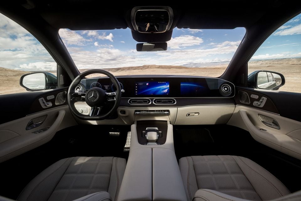 Painel do Mercedes-Benz GLE 450e híbrido plug-in 2026 com tela dupla, volante e bancos dianteiros de couro bege, cenário desértico lá fora