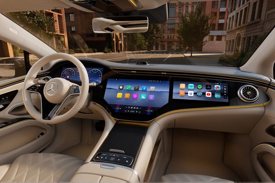 Interior of a 2026 Mercedes-Benz EQS 400 sedan showing the large dual-screen MBUX infotainment display, cream leather seats, and three-spoke steering wheel