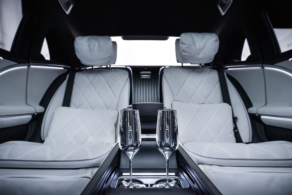 Luxurious rear cabin of a 2026 Mercedes-Maybach featuring white quilted leather seats and two crystal champagne flutes in the centre console