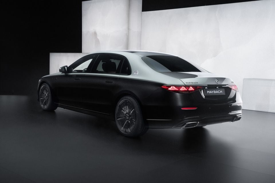 A Mercedes-Maybach S-Class sedan seen from the rear three-quarter angle in a dark studio, finished in a two-tone black and silver colour scheme
