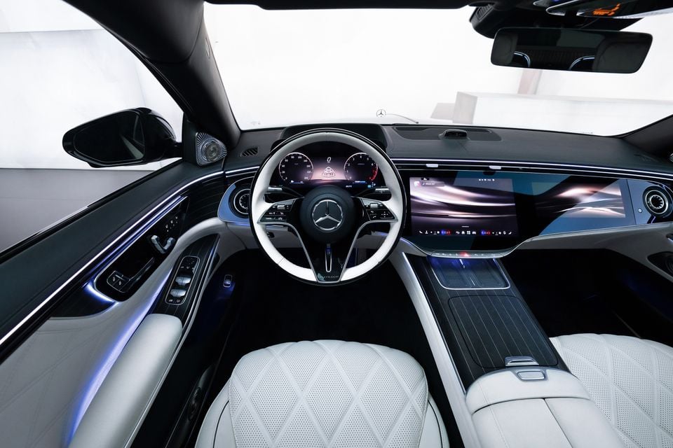 Interior of a Mercedes-Maybach showing the white quilted leather seats, two-tone steering wheel with Maybach branding, digital instrument cluster, and large central infotainment touchscreen