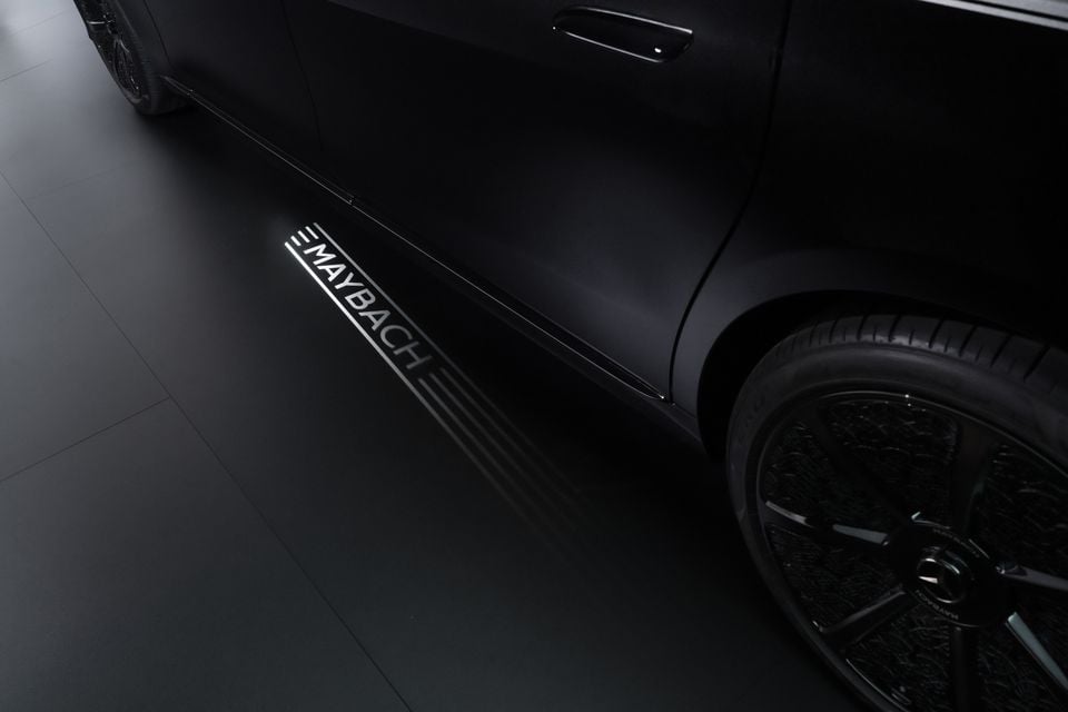 Close-up of a Mercedes-Maybach illuminated puddle light projecting the Maybach logo onto the ground beneath the door sill of a black luxury car.