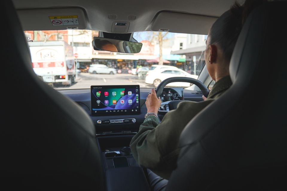 A driver operates the touchscreen infotainment system in a 2026 MG4 EV while driving through a city street.