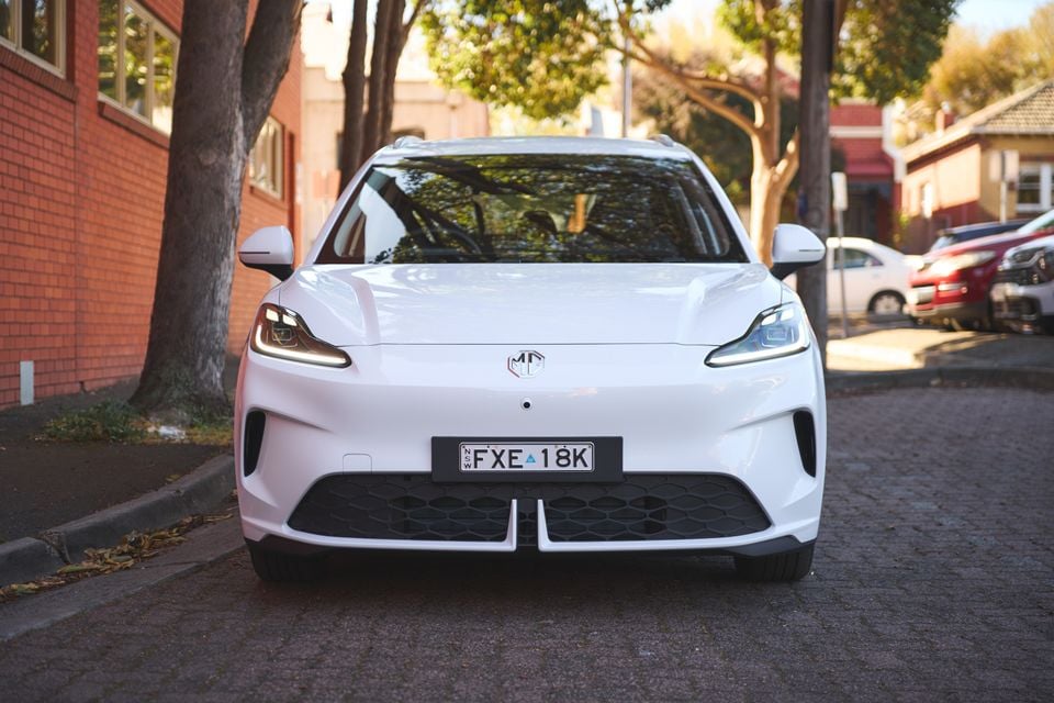 A white 2026 MG4 EV hatchback parked on a residential street, viewed head-on