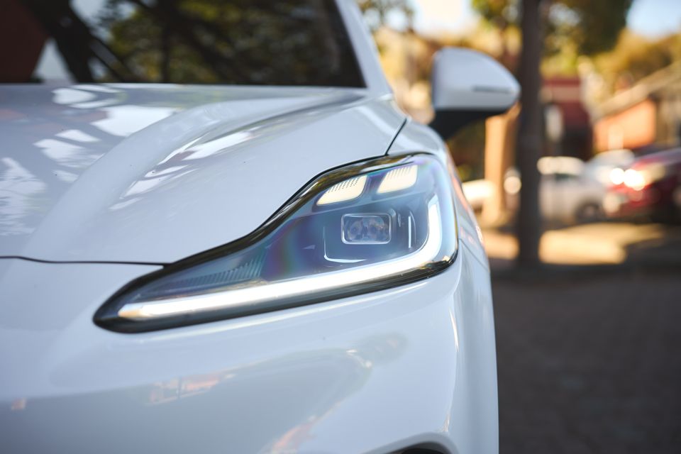 Close-up of the headlight on a white 2026 MG4 EV hatchback, with the wing mirror visible in the background.