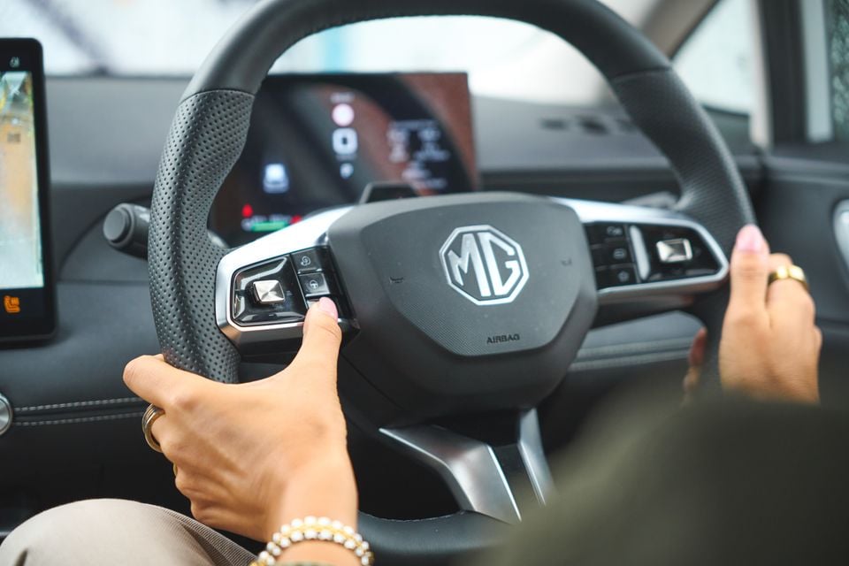 A person's hands grip the steering wheel of a 2026 MG4 EV, showing the MG badge and dashboard display