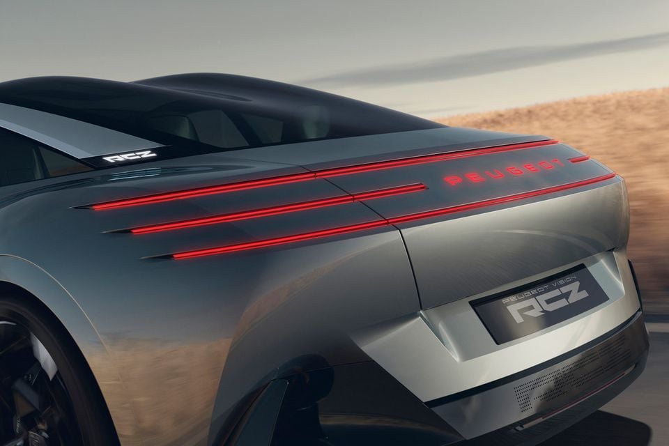 Rear of the silver 2026 Peugeot Vision RCZ concept in motion, showing its red light-bar tail-lights, illuminated Peugeot lettering and RCZ badge