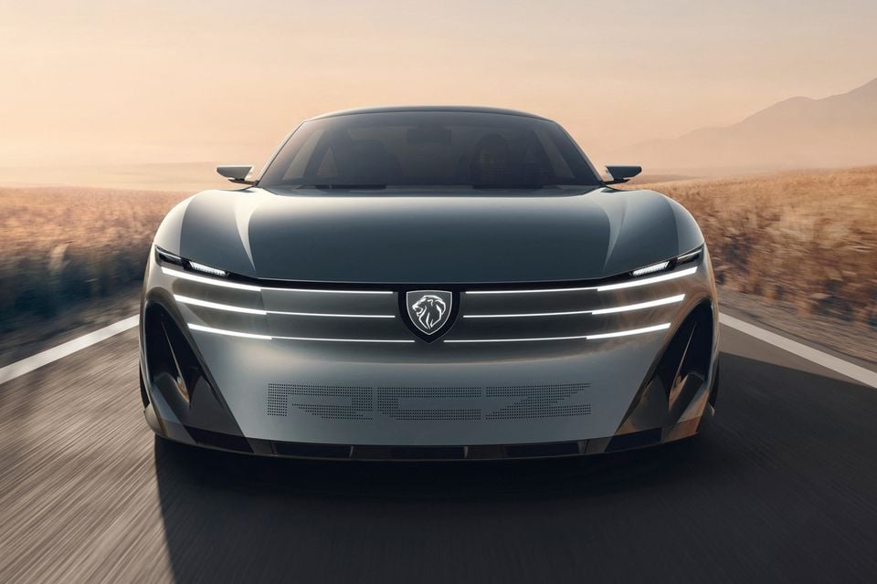 The 2026 Peugeot Vision RCZ concept, a silver coupe with a light-bar front end and lion badge, driving towards the camera on a desert road