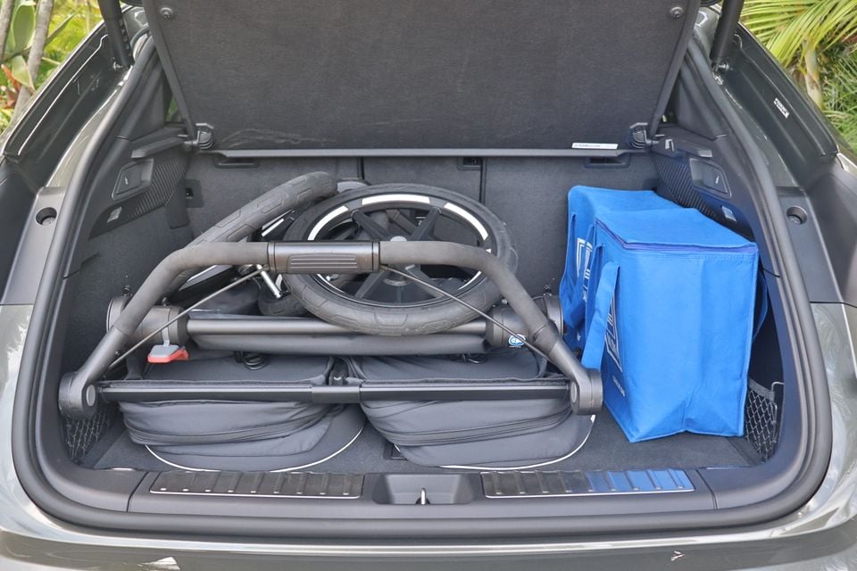 The open boot of a Porsche Macan loaded with a folded pram and a blue shopping bag, showing available cargo space.