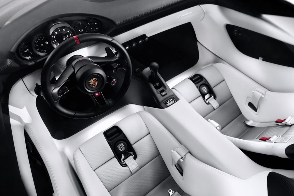 Cockpit of the 2026 Porsche Mission E concept, showing a black steering wheel, round analogue gauges, a centre gear lever and white sports seats with harnesses.