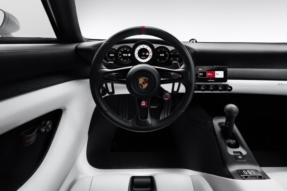 Cabin of the Porsche Mission E concept with a black steering wheel, round digital gauges, small touchscreen and white leather trim