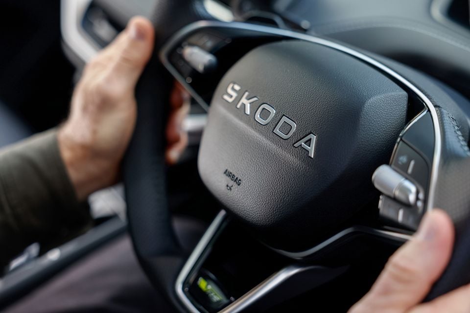 Close-up of a Skoda Enyaq steering wheel being held by a driver, showing the Skoda logo and steering wheel controls.