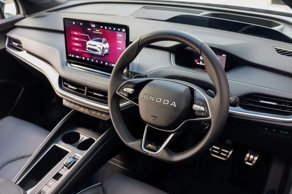 Interior of a Skoda Enyaq RS showing the steering wheel with RS badge and a large touchscreen infotainment display on the dashboard, right-hand drive