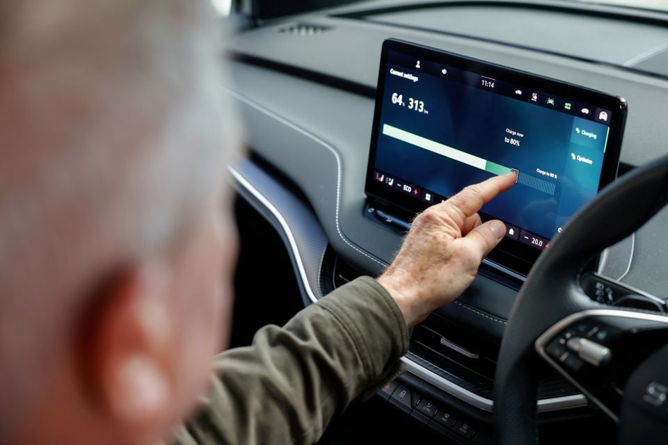 A person touching the infotainment touchscreen inside a Skoda Enyaq, showing battery charge settings with 313km of range displayed