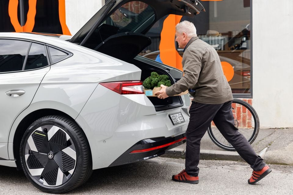A man loading groceries into the open boot of a silver 2026 Skoda Enyaq outside a shop