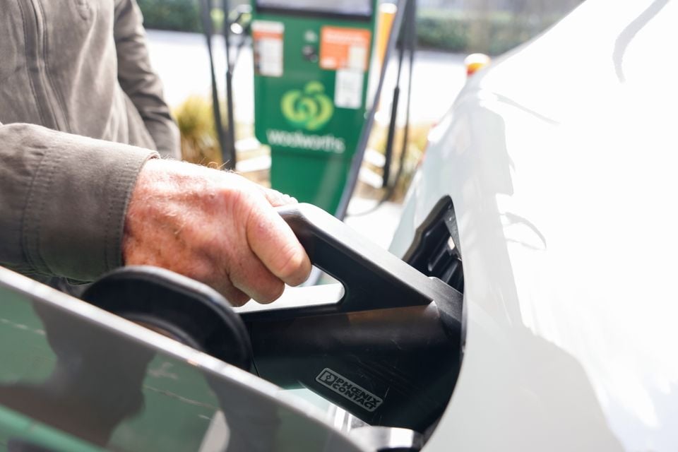 A person plugging an EV charging connector into a white electric car at a Woolworths charging station in Australia