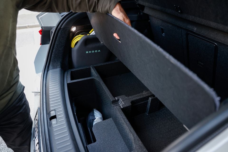 The under-floor storage compartment of a Skoda Enyaq boot, lifted open to reveal a Skoda-branded charging cable bag and additional storage sections.